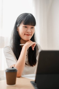 Evde elinde kahve fincanıyla dizüstü bilgisayar kullanan genç bir kadın, parlak ve modern bir ortamda verimli bir çalışma seansının keyfini çıkarıyor..