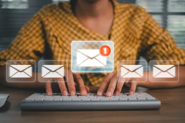 Eller dijital e- posta simgeleri ve uyarıları olan bir klavyeye yazarak, modern ofis ortamında e-posta pazarlama kavramını resmediyor.