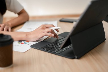 Veri analizi için tablet ve stil kullanan ellerin yakın plan fotoğrafı. Tahta bir masanın üzerinde kahve ve belgeler var..