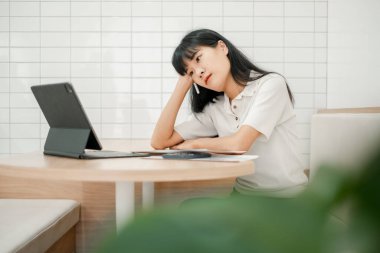 Beyaz gömlekli genç bir kadın modern bir kafede tablet kullanıyor. Minimalist tasarımı ve beyaz fayanslı duvarı var..