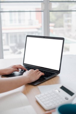 Eller boş bir ekranla dizüstü bilgisayarda yazarken, pencerenin yakınındaki ahşap bir masaya yerleştirilirken, parlak ve modern bir çalışma alanı yaratıyor..