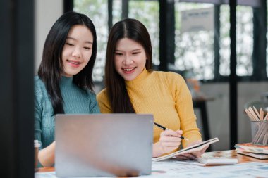 İki kadın bir projede birlikte çalışıyor, dizüstü bilgisayar kullanıyor ve parlak, modern ofis ortamında notlar alıyor..