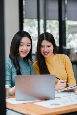 Dizüstü bilgisayarda birlikte çalışan iki genç kadın parlak ve modern ofis ortamında fikirleri tartışıyor..