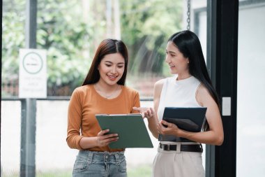 İki genç kadın, modern ofis ortamında dijital tabletler kullanarak bir tartışmaya giriştiler..