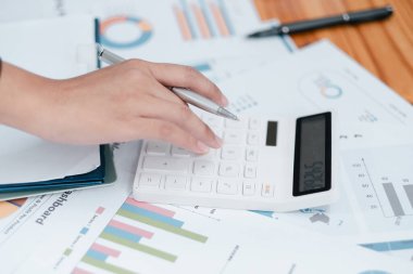 Finansal belgelerde hesap makinesi kullanan, veri analizi ve bütçe planlamasını gösteren bir elin yakın plan çekimi.