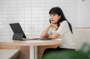 Beyaz fayanslı duvar ve ahşap mobilyaların yer aldığı şık bir kafe ortamında tablet kullanan odaklanmış bir kadın..