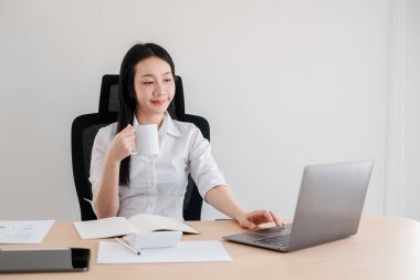 Ev ofis ortamında kendine güveni tam bir kadın, dizüstü bilgisayar kullanıyor ve kahve molası veriyor..