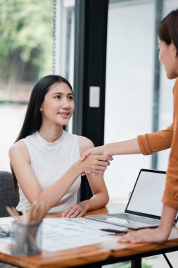 Modern bir ofiste el sıkışan iki kadın, başarılı bir iş anlaşmasını veya ortaklığı simgeliyor..