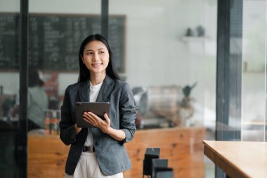 Modern ofis ortamında profesyonel bir kadın elinde tabletle güvenle gülümsüyor..