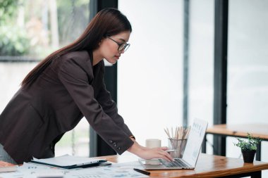 Ofisteki profesyonel kadın bilgisayardaki verileri analiz ediyor, modern bir çalışma alanında iş ve teknoloji sergiliyor..