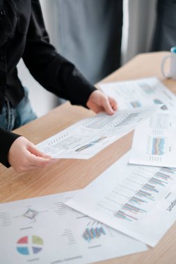 Finansal belgeleri renkli grafik ve grafiklerle inceleyen bir kişi, modern ofis ortamında veri analizini sergiliyor.