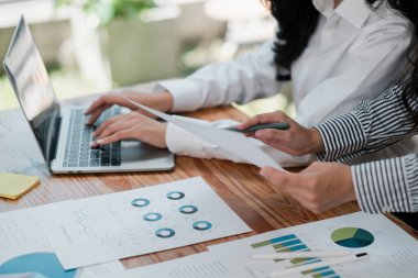 Finansal grafikleri ve grafikleri inceleyen iş adamları, modern bir ofis ortamında iş birliği yaparak bir dizüstü bilgisayar ve kağıt üzerinde çalışıyorlar..