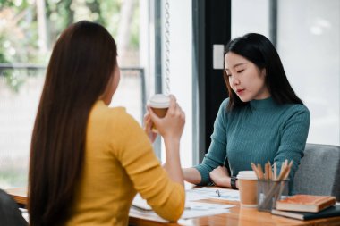 Modern bir kafede iş görüşmesi yapan iki kadın, kahve içerken fikir alışverişinde bulunuyorlar..