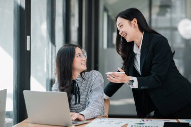 İki iş kadını, parlak ve modern bir ofis ortamında laptoplar ve evrak işleriyle ortak bir tartışmaya giriştiler..