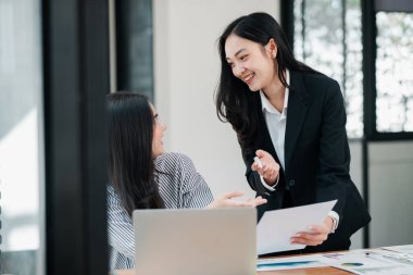 Çağdaş bir ofis ortamında belgeleri tartışan iki iş kadını ortak bir toplantı yaptılar..