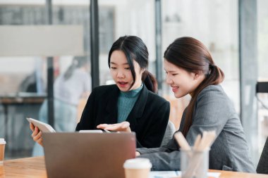 Çağdaş ofis ortamında dizüstü bilgisayar ve tablet kullanan iki iş kadını bir tartışmaya giriştiler..