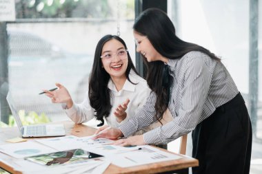 İki profesyonel kadın bir masa başında dizüstü bilgisayar ve belgelerle takım çalışması ve işbirliği hakkında tartışıyorlar..