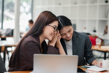Modern bir ofiste iki iş kadını, bir proje üzerinde birlikte çalışıyorlar, fikirleri paylaşıyorlar ve gülümsüyorlar, takım çalışması ve işbirliği sergiliyorlar..