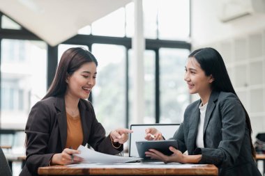 İki iş kadını, parlak, modern bir ofis ortamında, takım çalışması ve işbirliği sergileyerek bir masada çalışmayı tartışıyor..