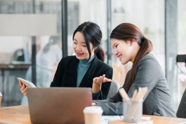 Çağdaş bir ofiste çalışmayı tartışan iki iş kadını, işbirliği için bir laptop ve tablet kullanıyorlar..
