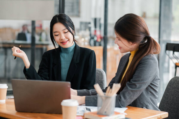 Две деловые женщины обсуждают работу за ноутбуком в современной офисной среде, демонстрируют командную работу и производительность.