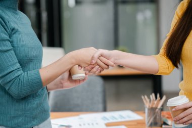 Ofiste tokalaşan iki kadın, takım çalışmasını ve işbirliğini sembolize ediyor, kahve fincanları ve görünür belgelerle.
