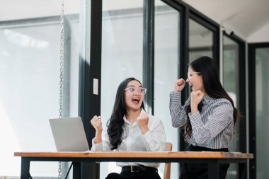 İki neşeli iş kadını, bilgisayar ve cam duvarlarla çağdaş ofis ortamında başarıyı kutluyor..
