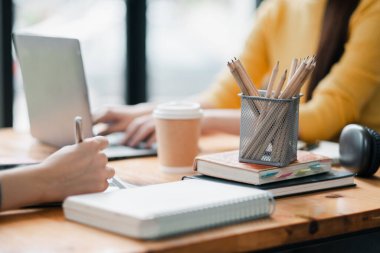 Dizüstü bilgisayarları, defterleri ve kahvesi olan modern bir ofis ortamında, ortak ve yaratıcı bir çalışma alanı sergileniyor..