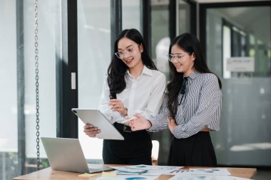 Çağdaş ofis ortamında bir tablet kullanarak proje detaylarını tartışan iki iş kadını.