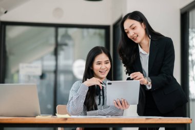 Modern ofis ortamında dijital tablet ve dizüstü bilgisayar kullanarak bir proje üzerinde çalışan iki profesyonel kadın..