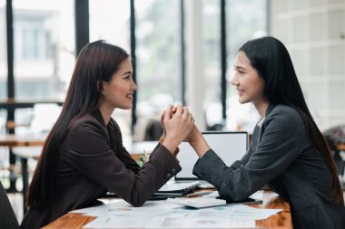 Modern ofis ortamındaki iki profesyonel kadın, bir iş görüşmesi sırasında pozitif ve işbirlikçi bir anı paylaşıyorlar..