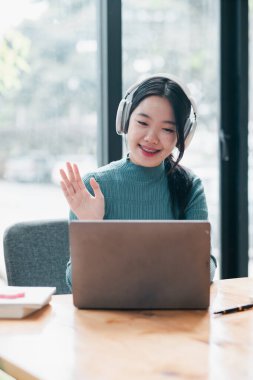 Parlak bir ofis ortamında bilgisayar ve kulaklık kullanan gülümseyen kadın..
