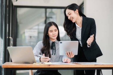 Modern ofis ortamında iki iş kadını dizüstü bilgisayarları ve tableti olan bir projede işbirliği yapıyor, takım çalışması ve yenilik sergiliyor.
