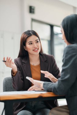 Modern bir ofis masasında iş görüşmesi yapan iki kadın, profesyonel etkileşim ve işbirliğini ön plana çıkarıyor..