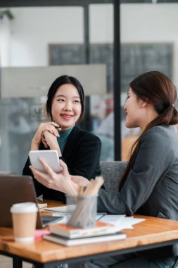 Modern ofis ortamında laptoplarla ve masada kahve ile iş tartışan iki kadın..