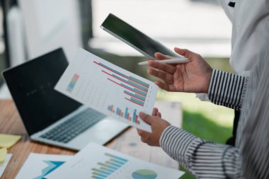 Modern bir ofis ortamında kağıt ve dijital cihazlar üzerinde finansal tablolar ve grafikleri inceleyen iki profesyonel.