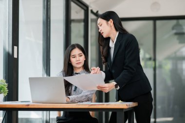 İki iş kadını modern ofis ortamında belgeleri tartışıyor, takım çalışması ve işbirliği sergiliyorlar..