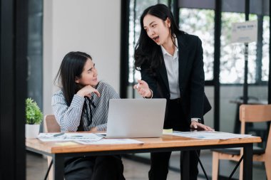İki iş kadını, modern ofis ortamında dizüstü bilgisayar ve belgelerle bir projeyi tartışıyorlar..