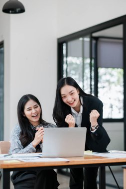 Modern bir ofiste laptopa bakarken başarıyı kutlayan iki neşeli iş kadını..
