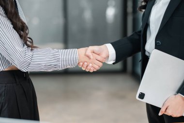 İki iş adamının el sıkışması, kurumsal bir ortamda ortaklık ve anlaşmayı sembolize eder..
