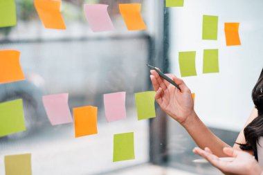 Modern ofis ortamında yaratıcı bir beyin fırtınası sırasında cam duvara renkli yapışkan notlar yerleştiren eller..