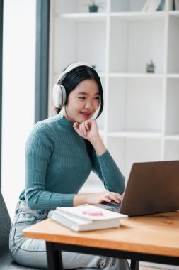 Kulaklık takan genç bir kadın, bilgisayarına odaklanmış, parlak ve modern bir ofis ortamında çalışıyor..