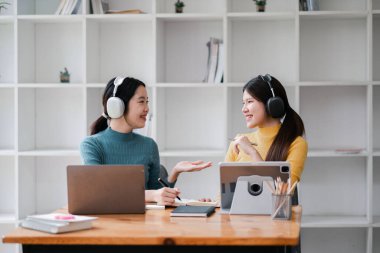 Modern ofis ortamında dizüstü bilgisayar ve tablet kullanan, kulaklık takan ve canlı bir tartışmaya giren iki kadın..