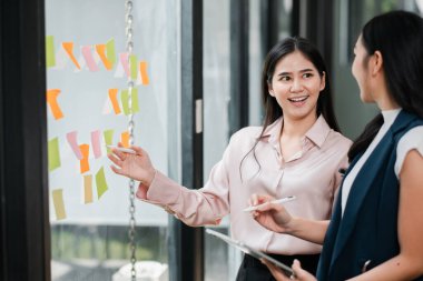 Çağdaş ofis ortamında fikirleri tartışan iki profesyonel kadın beyin fırtınası için renkli yapışkan notlar kullanıyorlar..