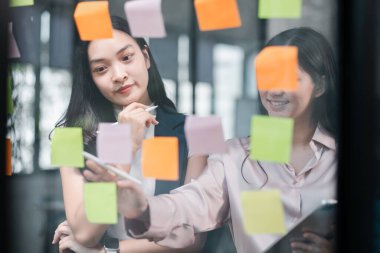 Bir ofiste işbirliği yapan iki kadın beyin fırtınası ve proje planlaması için renkli yapışkan notlar kullanıyor..
