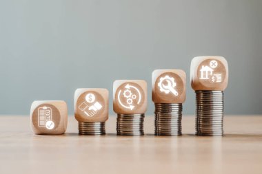 İstiflenmiş paralar üzerindeki tahta bloklar varlık yaşam döngüsü evrelerini gösteriyor, mali büyüme, yönetim ve yatırım stratejilerini sembolize ediyor.