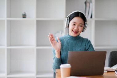 Ev ortamında sanal bir toplantı için dizüstü bilgisayar ve kulaklık kullanan gülümseyen kadın..