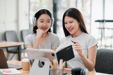 Modern ofis ortamında bir tablet ve defter kullanan iki genç kadın ortak bir çalışma seansına katıldı..