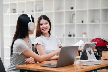 Modern bir ofis ortamında laptoplar ve kulaklıklar kullanarak birlikte çalışan iki genç kadın, ortak bir tartışma içindeler..