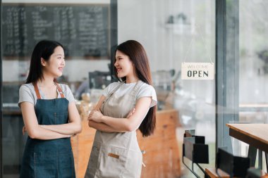 Modern bir kafede iki dost canlısı barmen, önlük giyiyorlar, kollarını kavuşturup açık bir tabelanın yanında birbirlerine gülümsüyorlar..